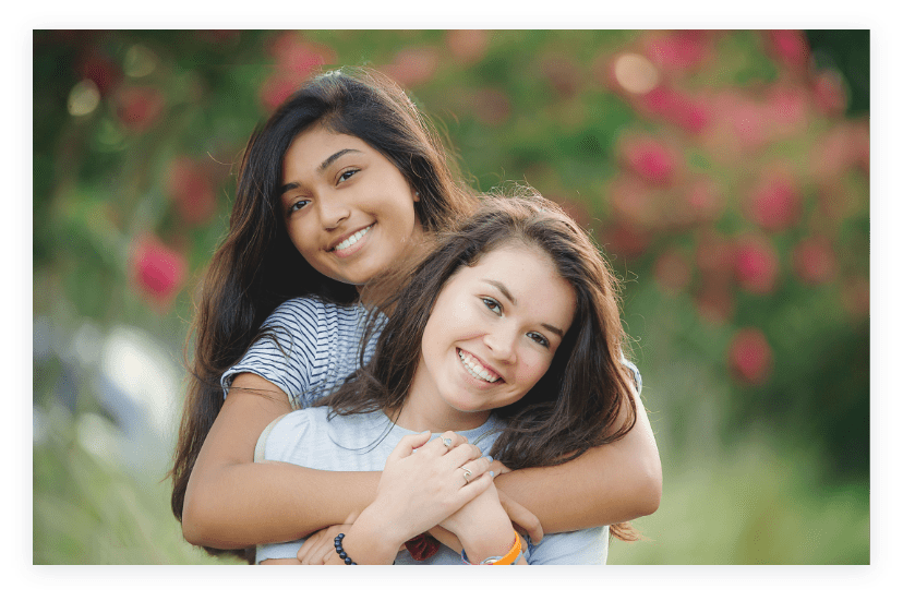 Image of two young girls with bright smiles hugging one another