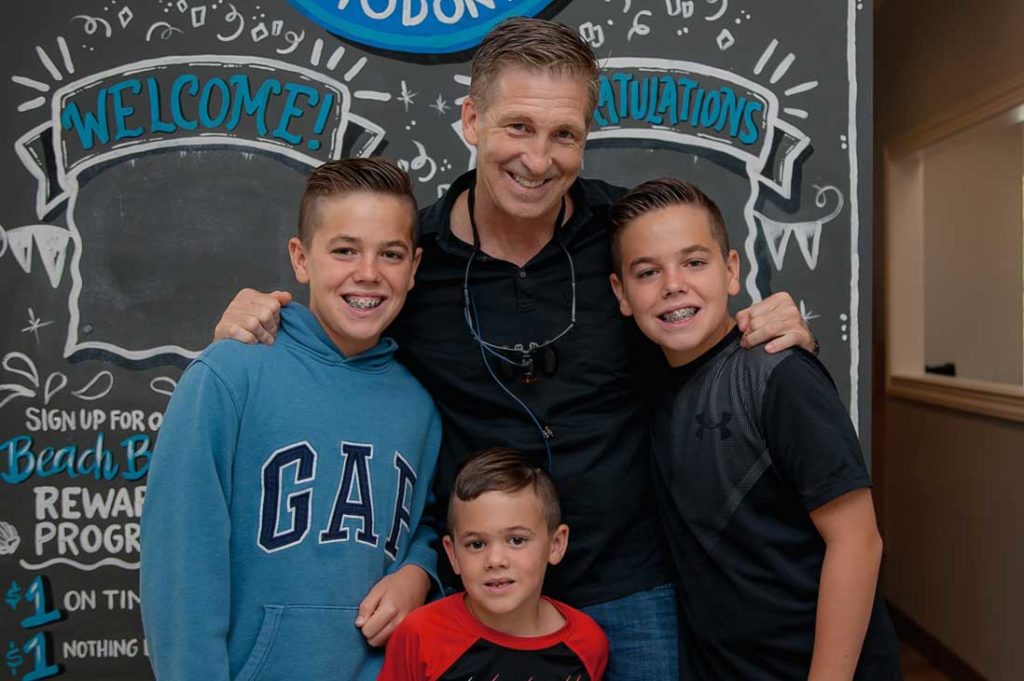 Photo of Dr. Henry with three young, smiling patients with braces.