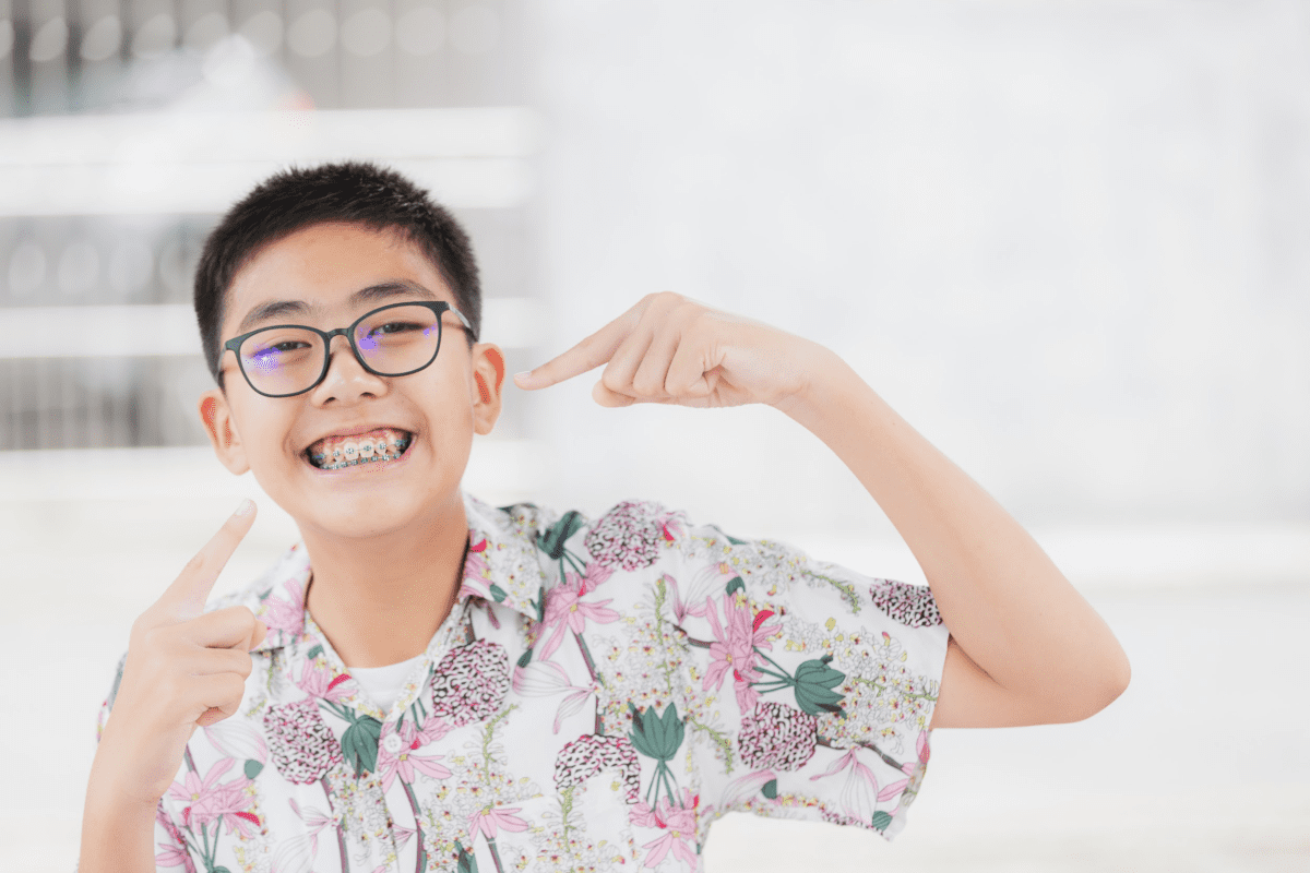 Image of boy with glasses smiling and pointing to his braces